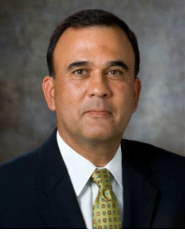 Anthony Santiago Man Smling with a suite on at the camera grey background and black suite