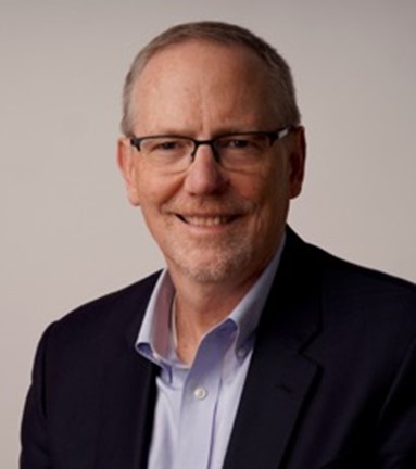 Tom Linton wearing glasses smiling at the camera with a grey back drop